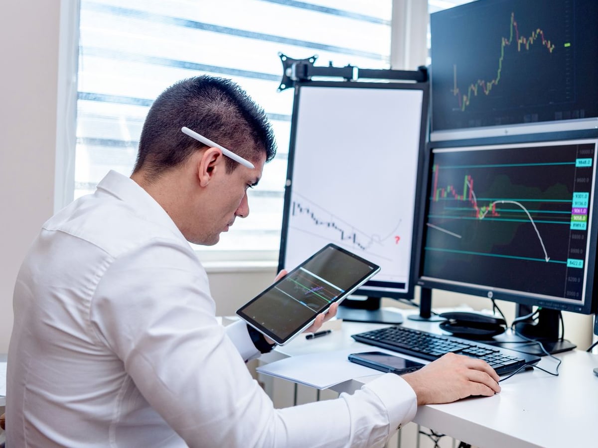 A trader reviewing forex charts across several monitors at a desk